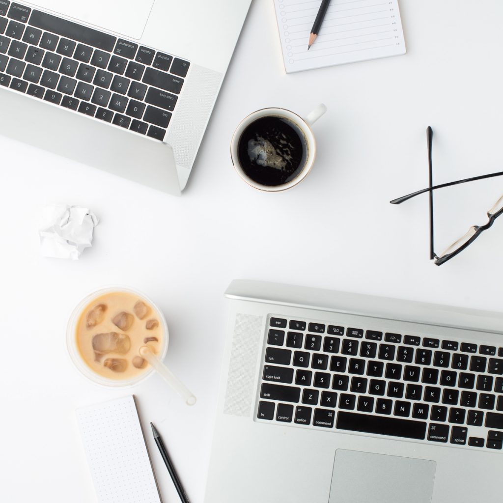 two laptops on a desk with ice and hot coffee, eyeglasses, and pens illustrating work on diy website mistakes to avoid